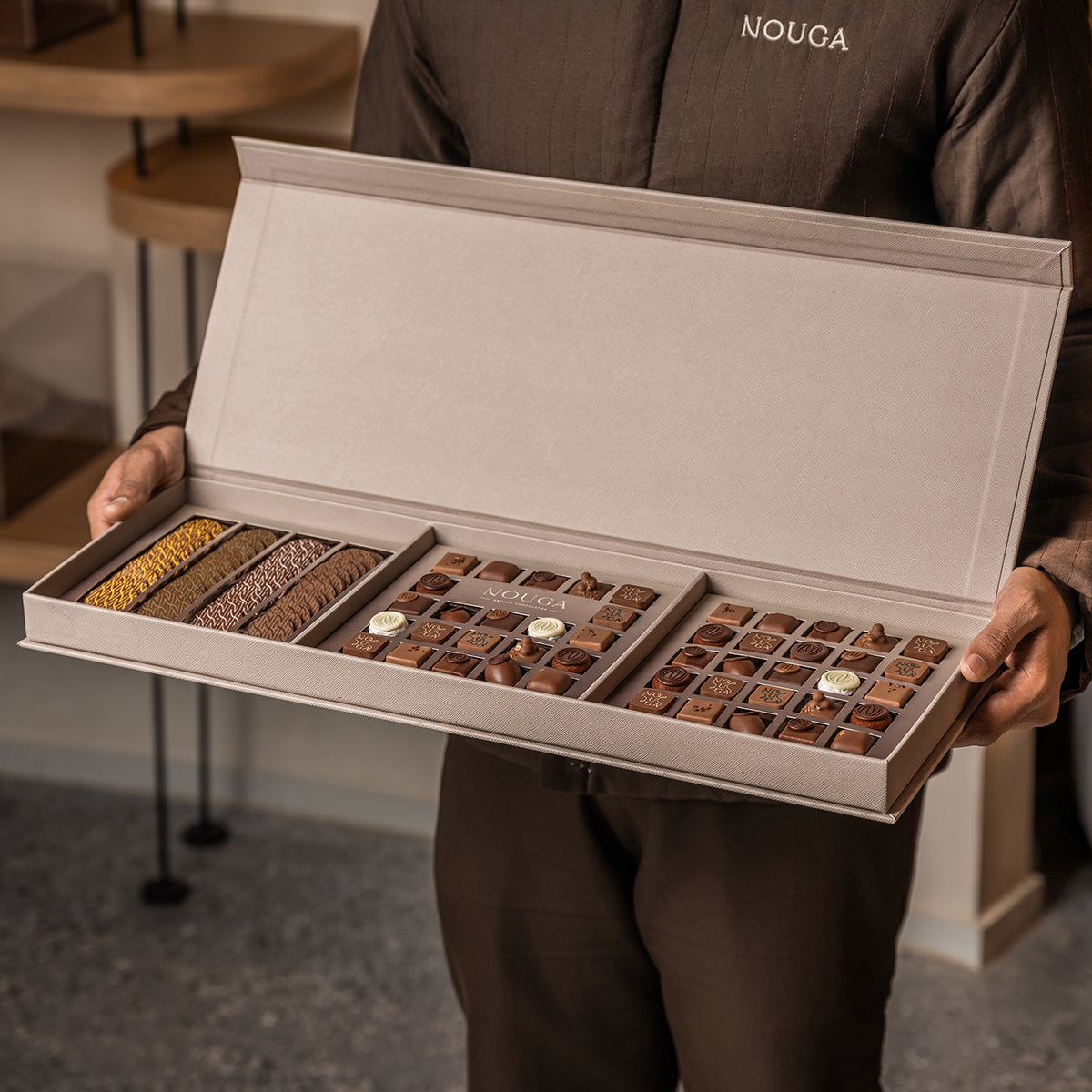 Person holding an open leather box of chocolates with 'NOUGA' branding.