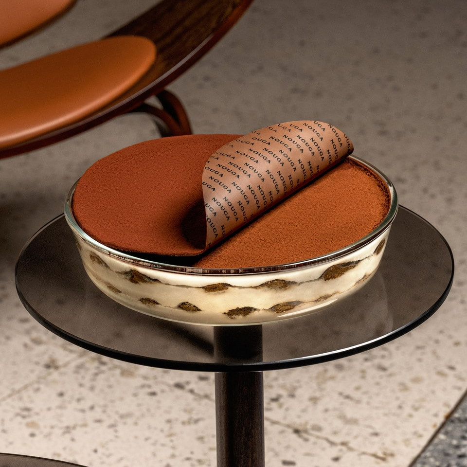 Small round table with a tiramisu on top, set against a neutral sophisticated background.