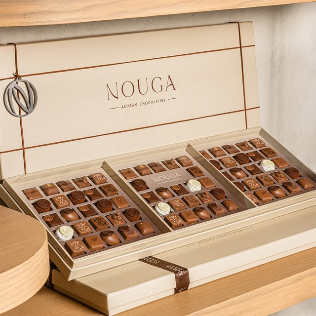 Open box of chocolates with 'Nouga' branding on a wooden surface.