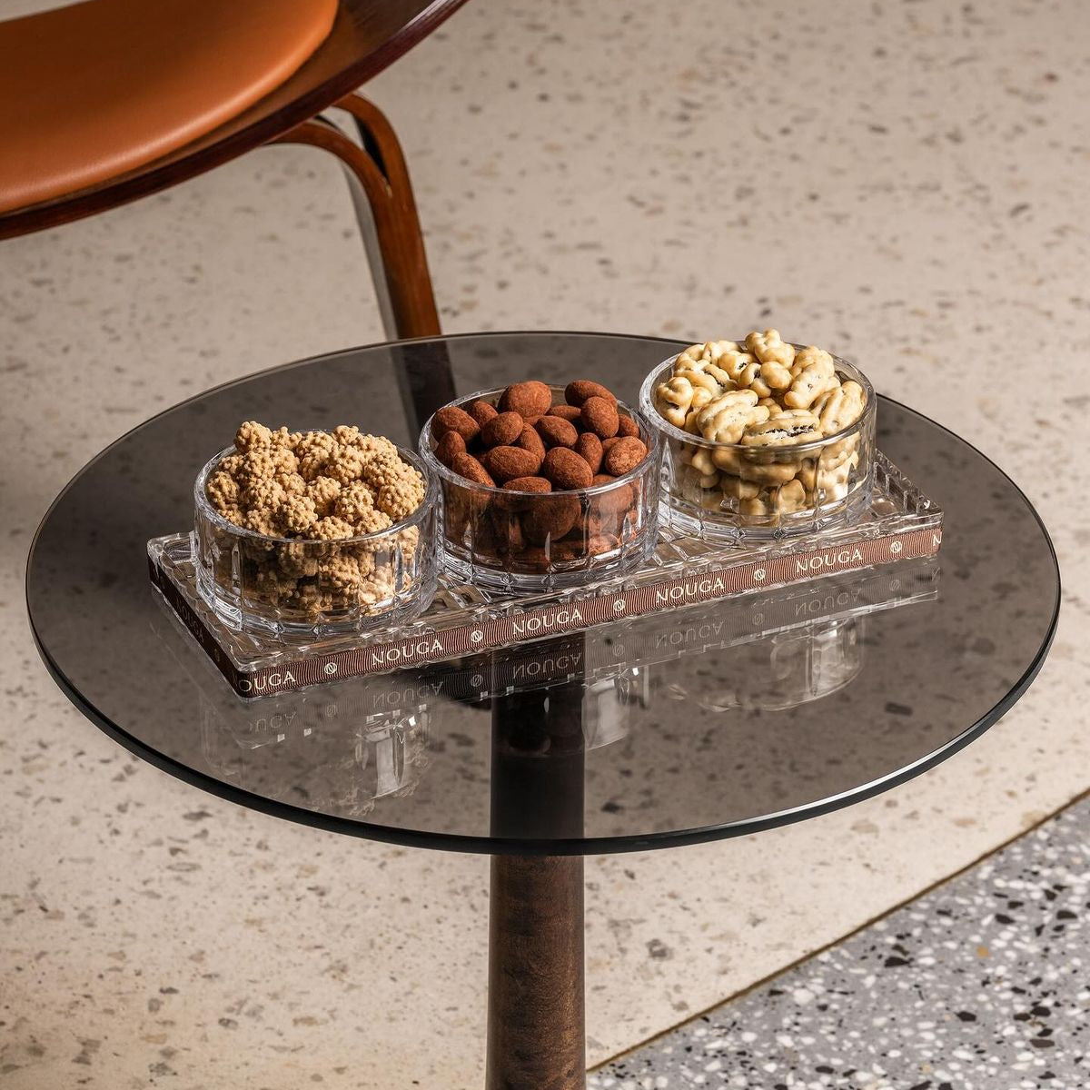 Small round table with glass top displaying three bowls of assorted dragees on a textured floor.