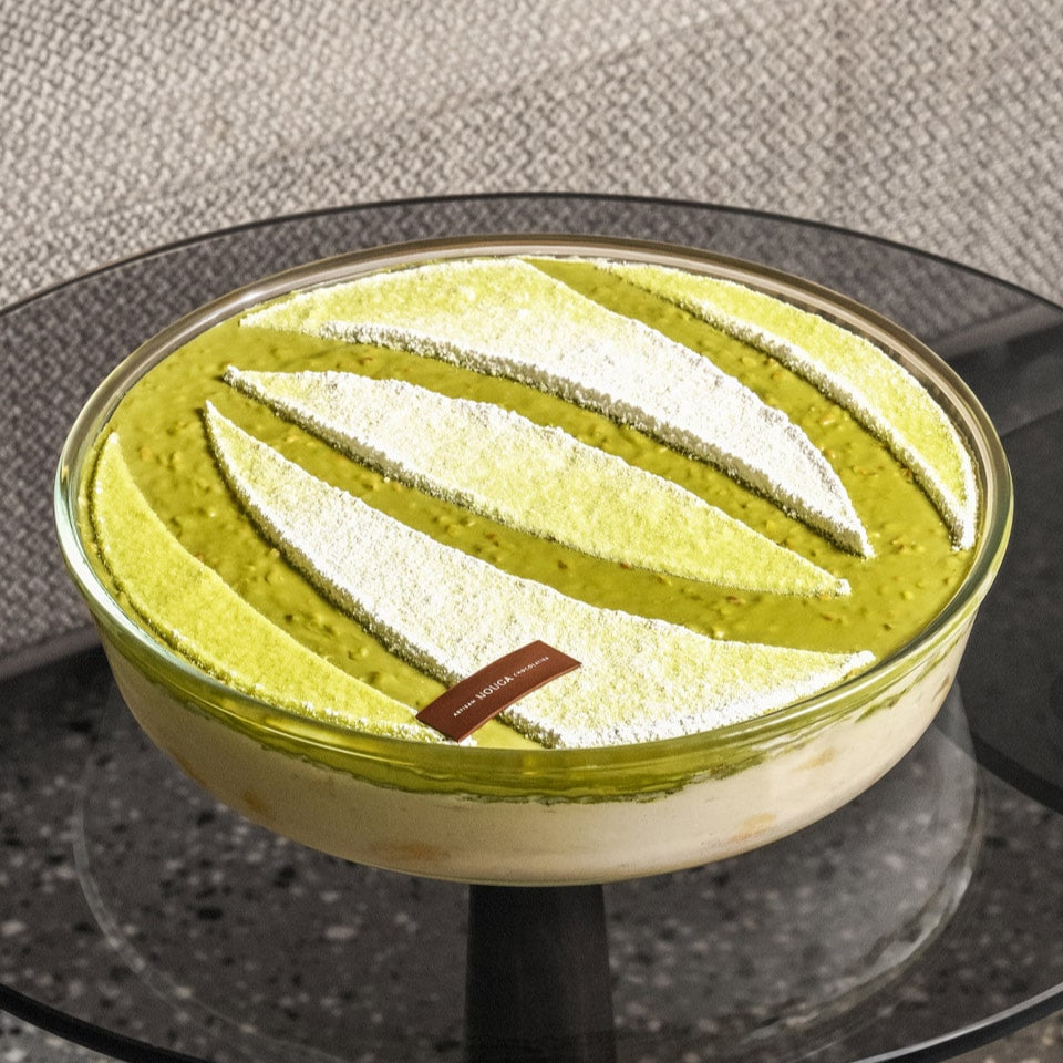 Green and white layered pistachio dessert tiramisu in a glass bowl on a gray glass surface.