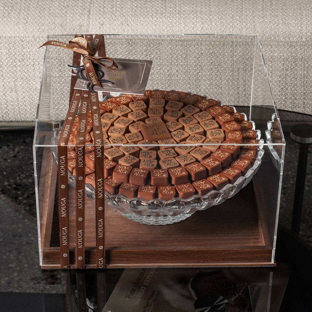 circular arrangement of chocolates on crystal tray in a clear and wooden box with a brand label.