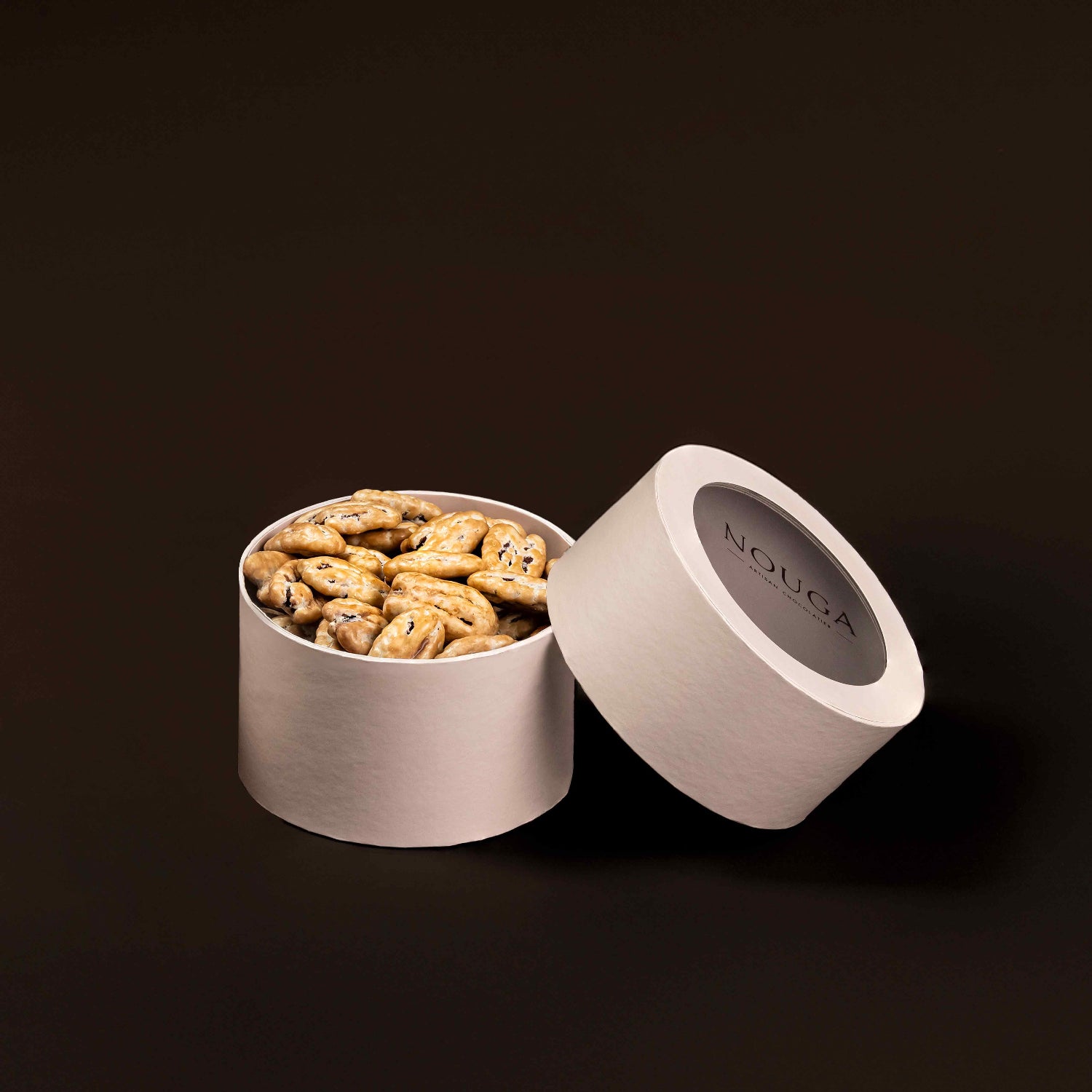 Open beige container with dulcey pecan dragees on a brown background, featuring the brand 'NOUGA'.