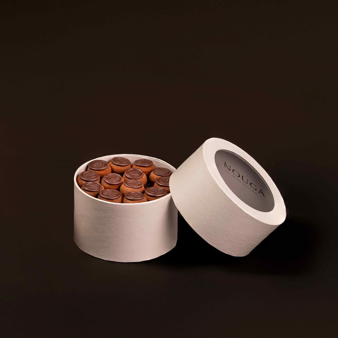Round beige box with chocolates and open lid on a dark background, featuring the brand 'NOUGA'.