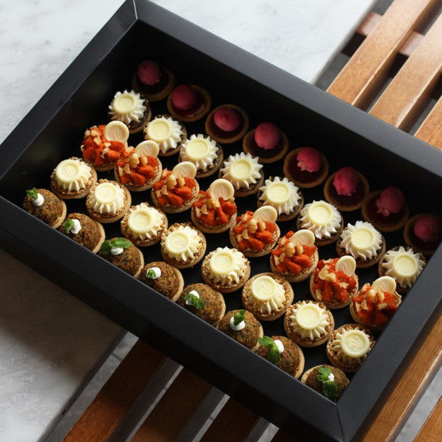 Assorted small canapés in a black rectangle box on a wooden and marble surface