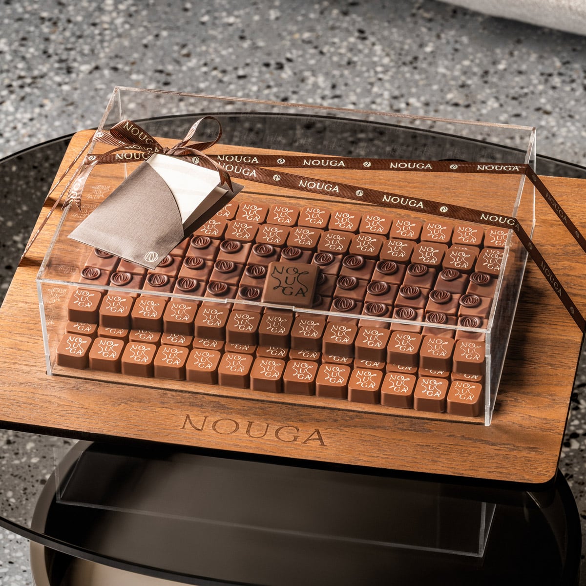 Tray with Nouga chocolate under clear lid on a wooden base