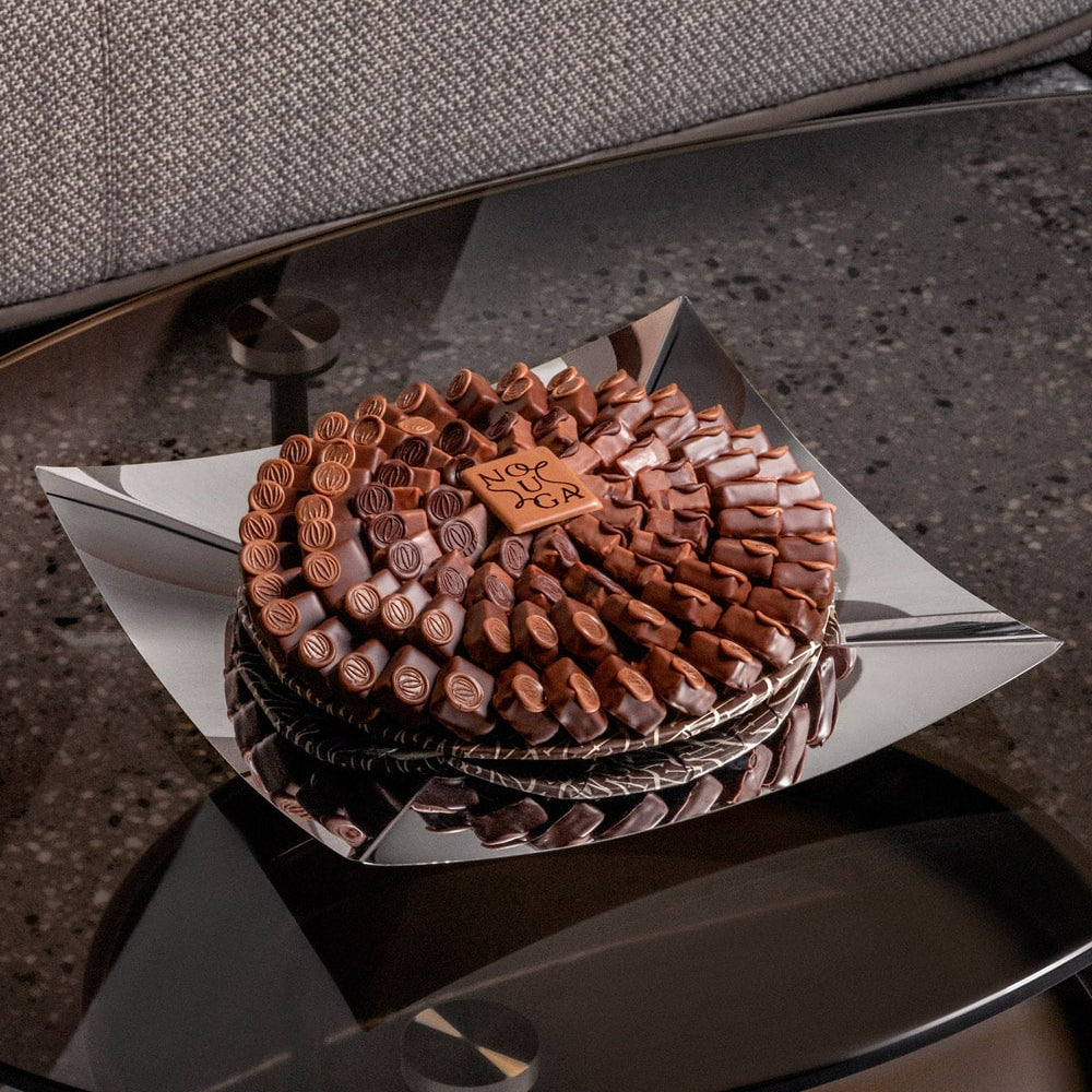 Square silver tray with chocolate bonbons on a reflective surface