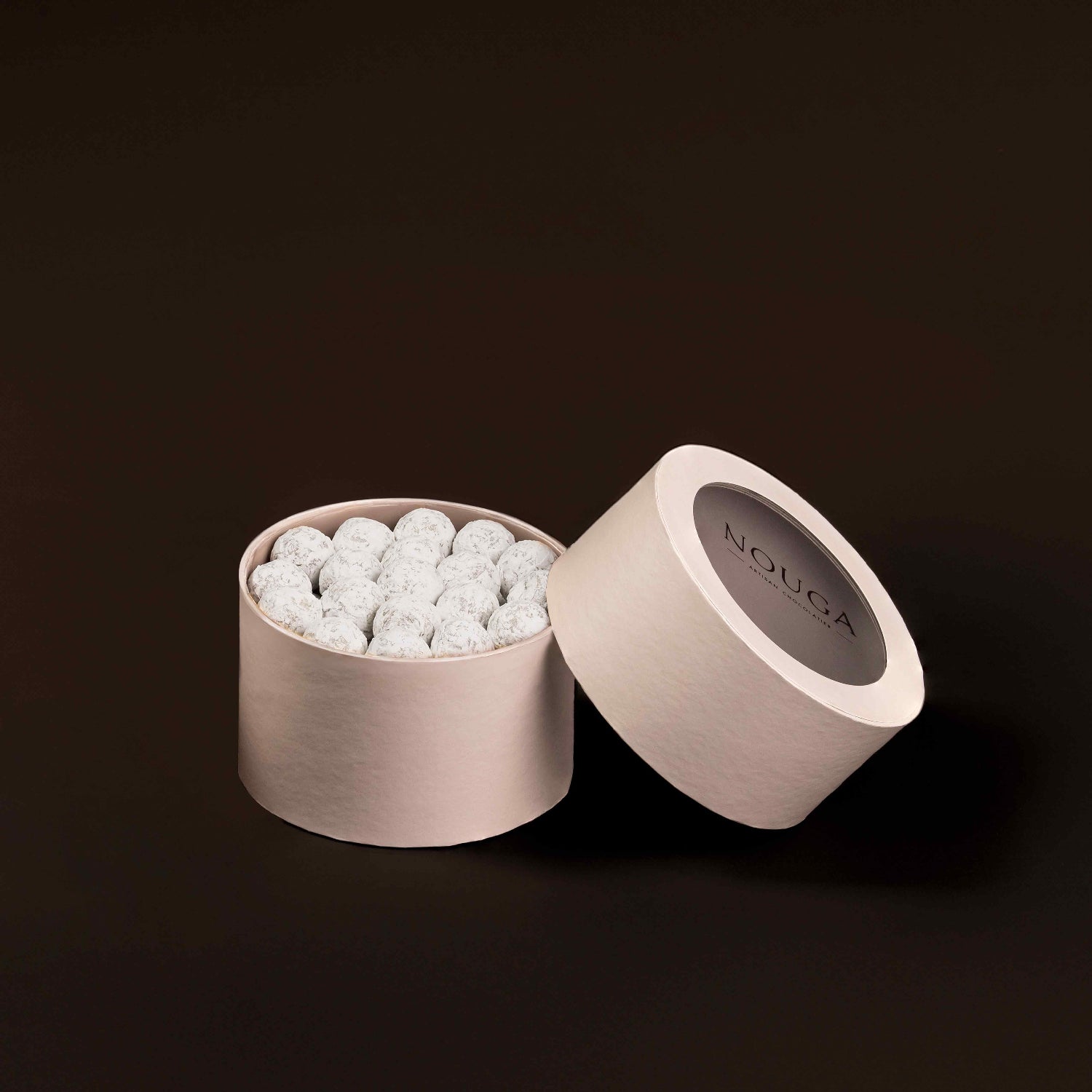 Open beige circle box with white caramel truffle, on a dark rbown background