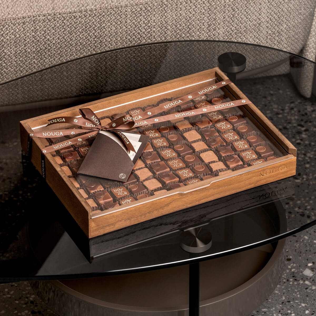 Wooden drawer box of chocolates with a ribbon on a glass table.