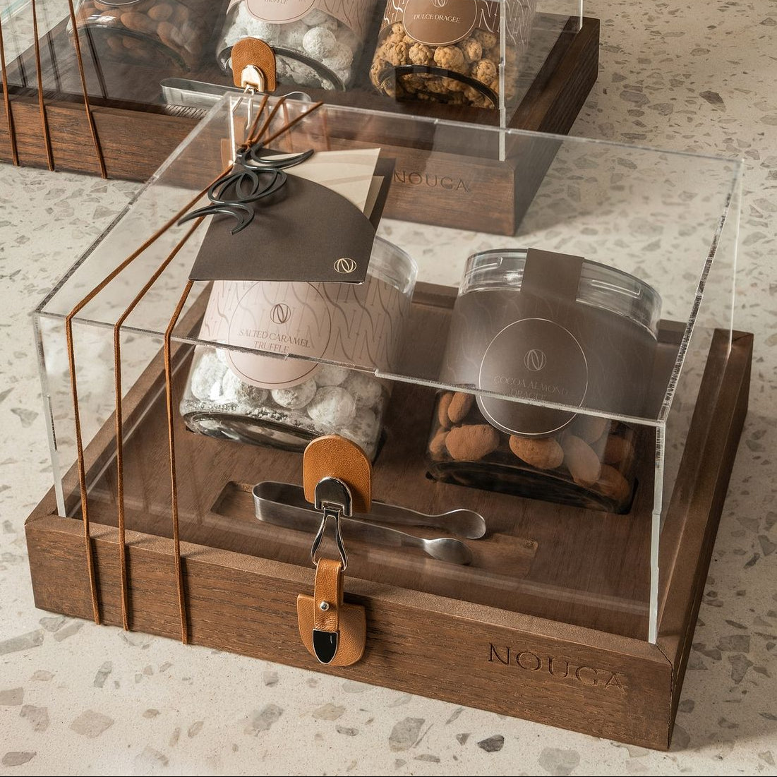 Wooden and glass display case with chocolate and dragees in luxury jars on a marble surface