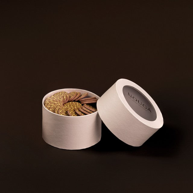 Open beige circle box with chocolate on a dark background, featuring the brand 'NOUCA'.