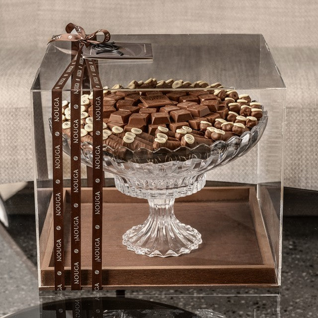Glass tray filled with assorted chocolates on a wooden base with 'Nouga' packaging.
