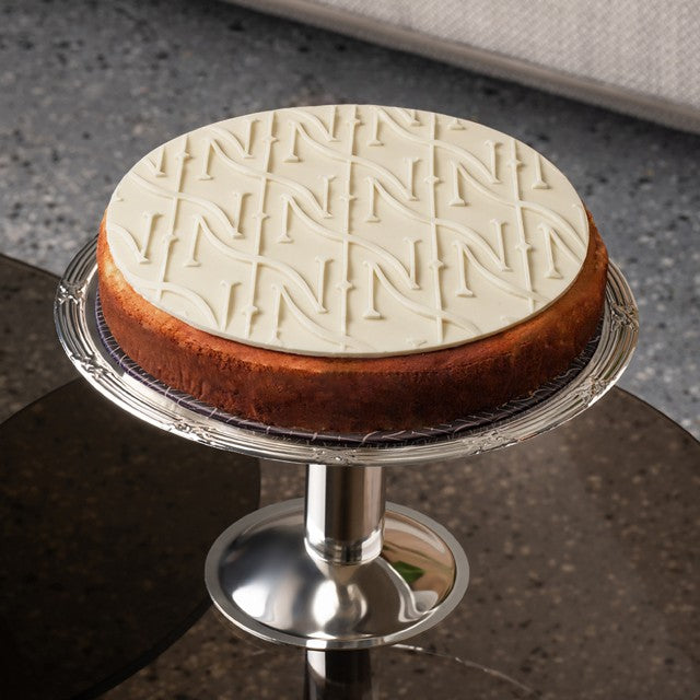 Cheesecake with white chocolate pattern lid on a silver cake stand