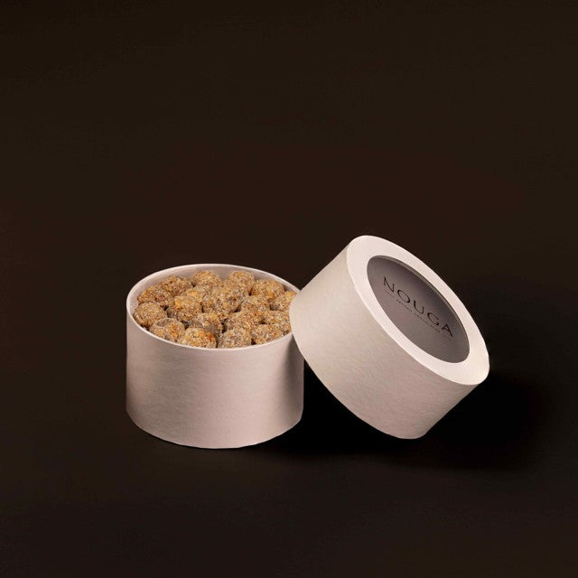 Open container of 'NOUGA' chocolates with visible coconut truffles inside on a dark background