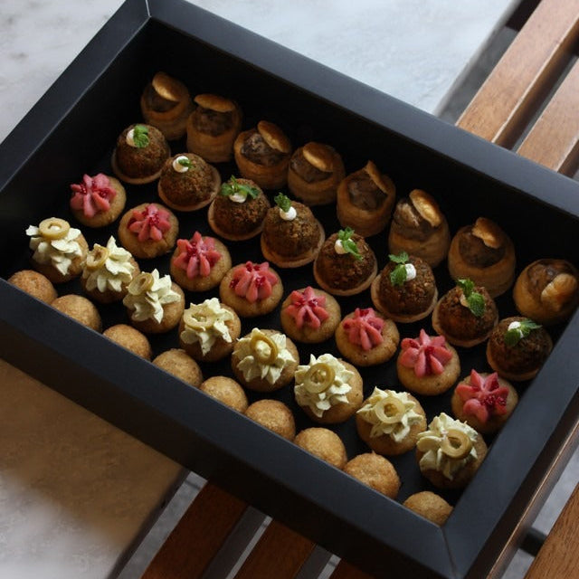 Assorted small canapés and pastries in a black box on a marble surface